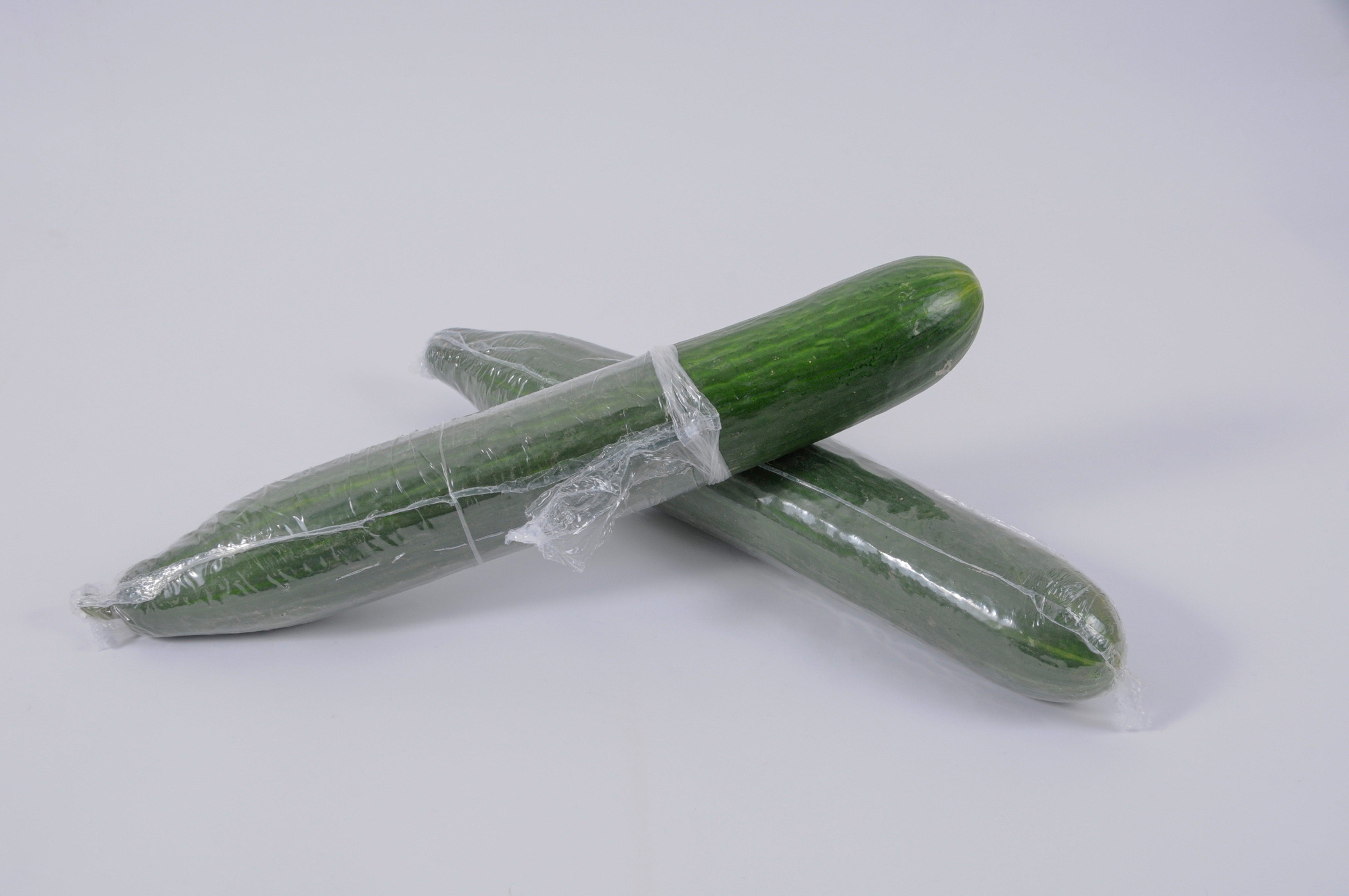 Zwei Salatgurken in Kunststofffolie verpackt. Eine Salatgurke ist zur H&auml;lfte ausgepackt