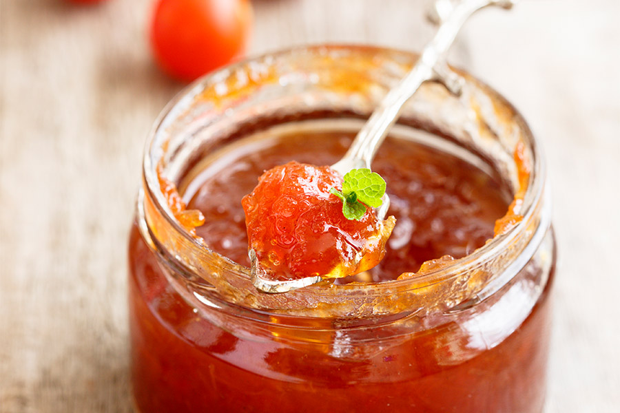 Marmeladeglas mit rötlichem Chutney. Ein Teelöffel Chutney, garniert mit frischem grünen Blatt, ragt aus dem Glas.