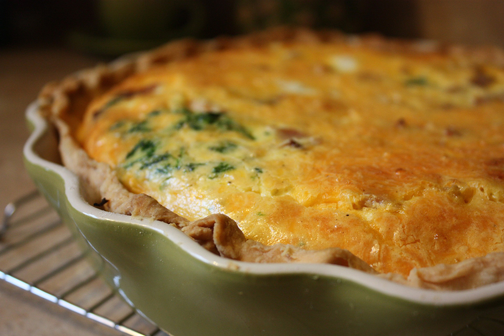 Goldbraune Quiche mit Mangold in der Füllung in einer hellgrünen Quicheform auf Backrohrrost.